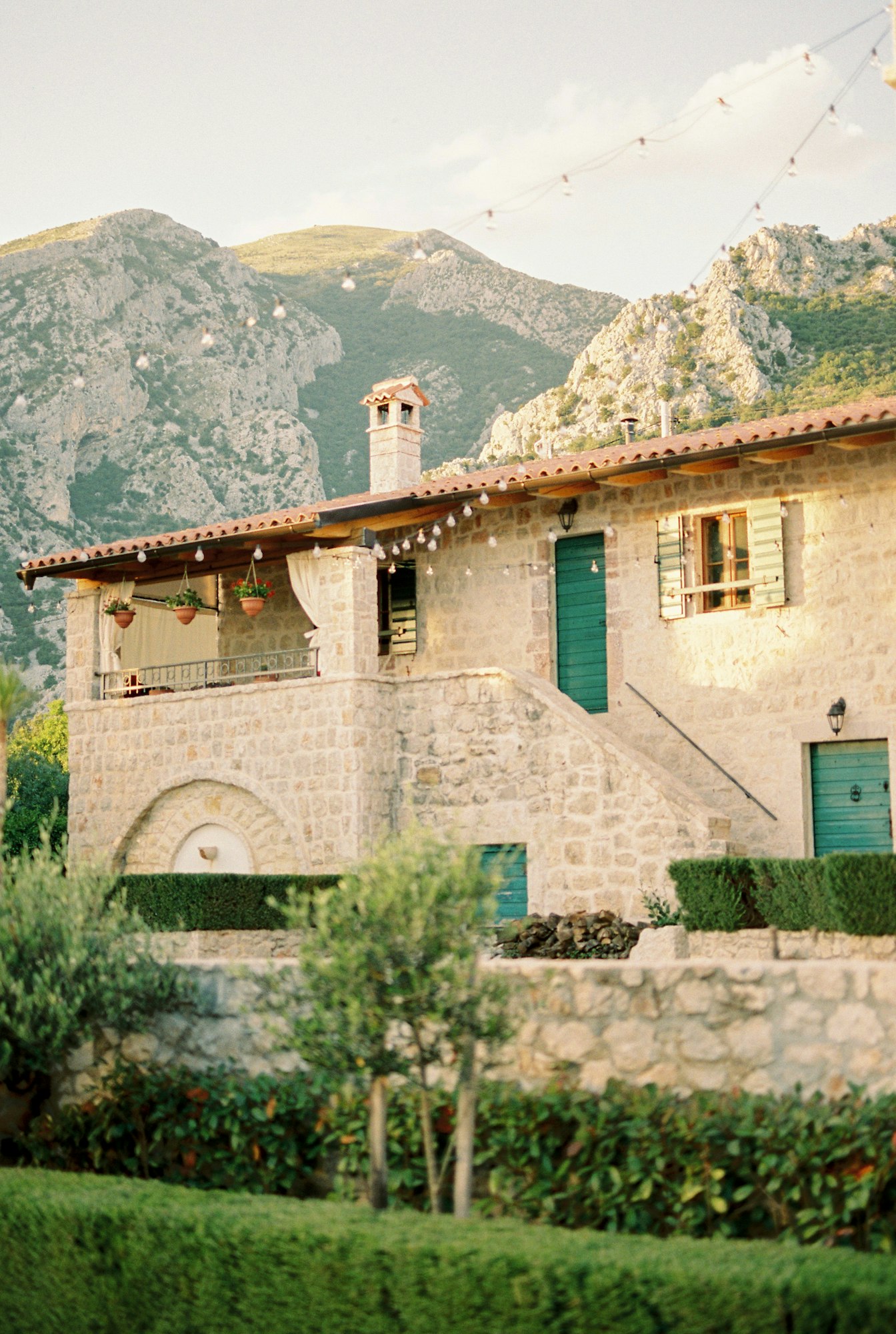 Cozy stone house with garlands of light bulbs in a green garden at the foot of the mountains